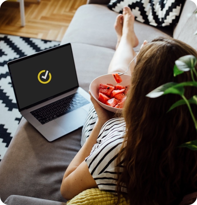 Frau auf dem Sofa mit Wassermelone und Laptop beim Starten von Norton 360 AntiVirus Plus